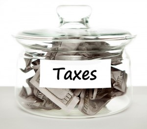 Black and white image of jar full of $100 bills and a sticker on the jar that says "Taxes". 